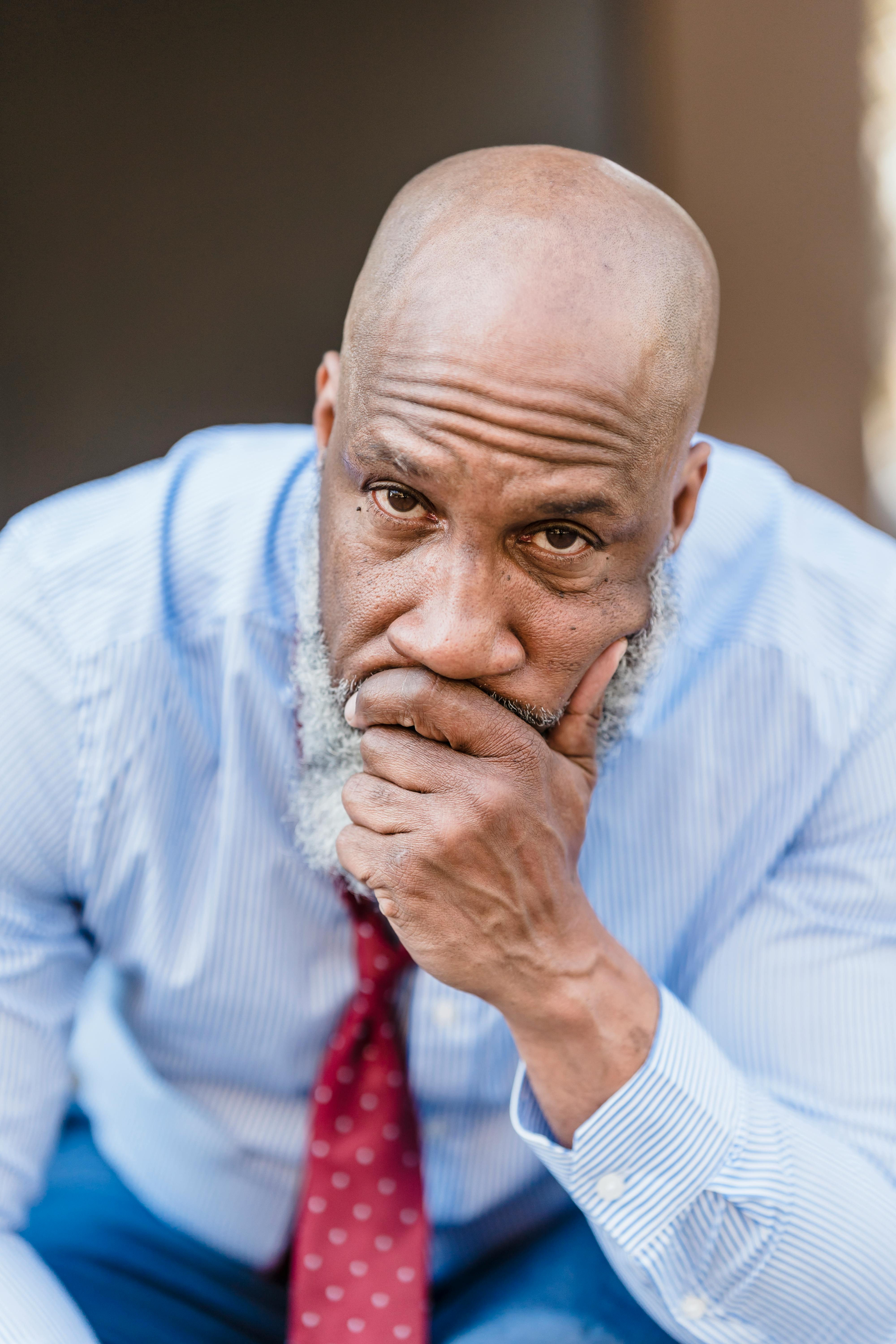 Thoughtful senior African American man in a blue shirt and red tie, expressing concern.