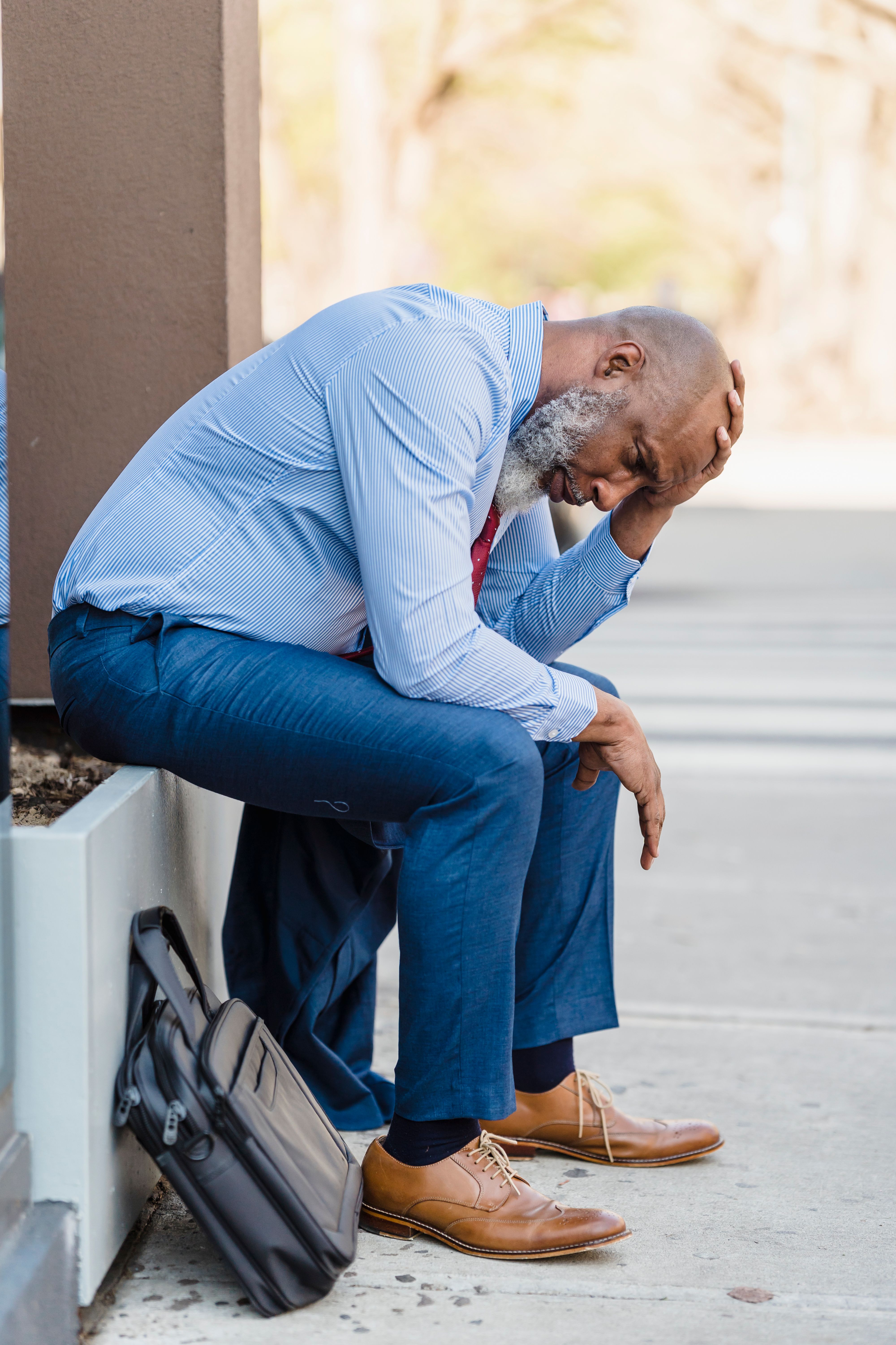 A worried senior businessman sitting on a bench, holding his head outdoors.