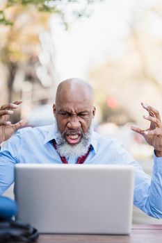 A frustrated African American man reacting to something on his laptop while sitting outdoors.