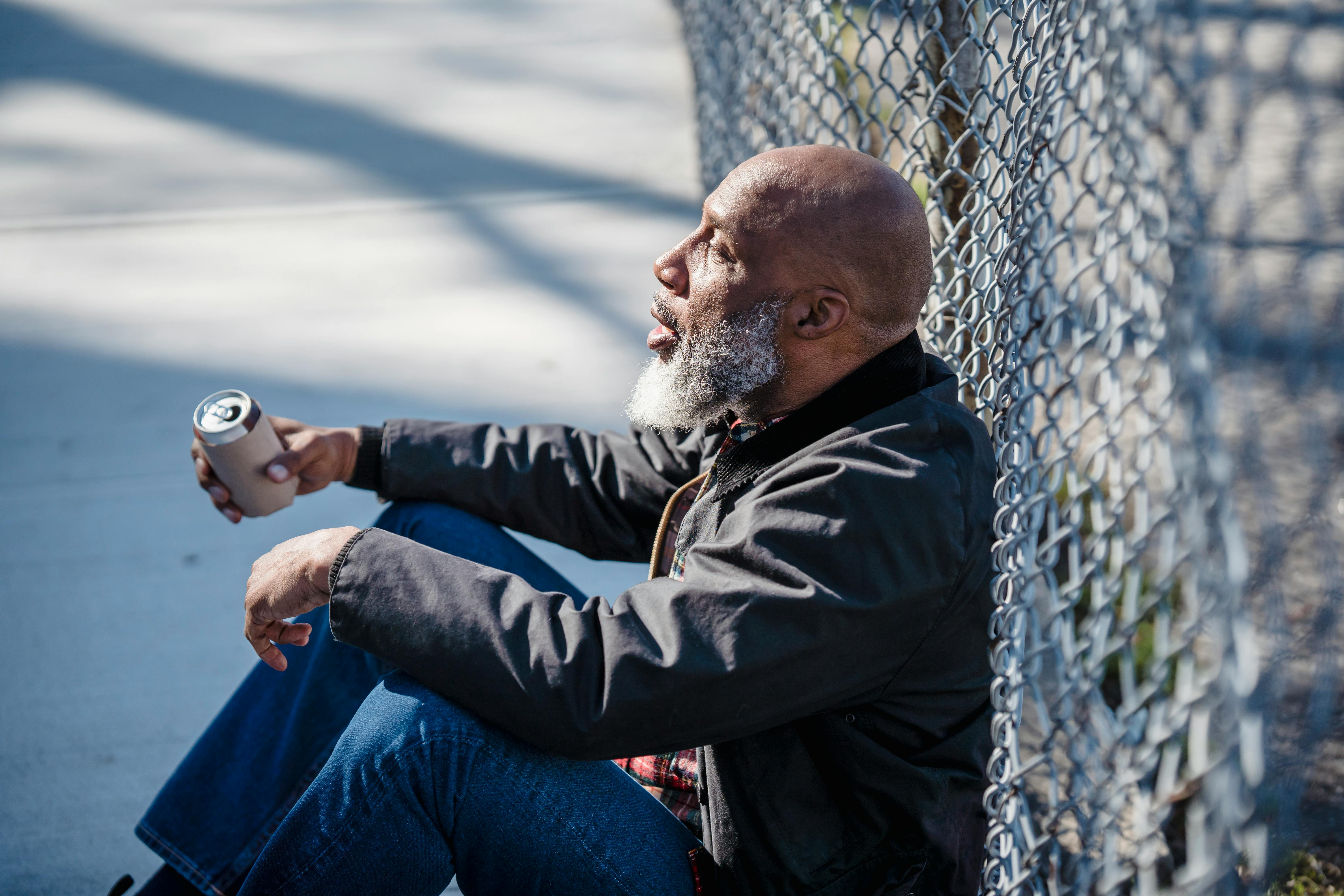 man in black jacket leaning on gray metal fence