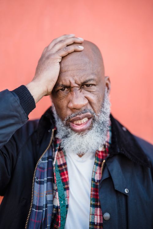 Free Portrait of an elderly bearded man with a thoughtful expression against a bright orange background. Stock Photo