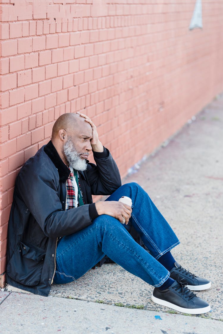 Distressed Old Man Sitting On Ground Drinking Beer