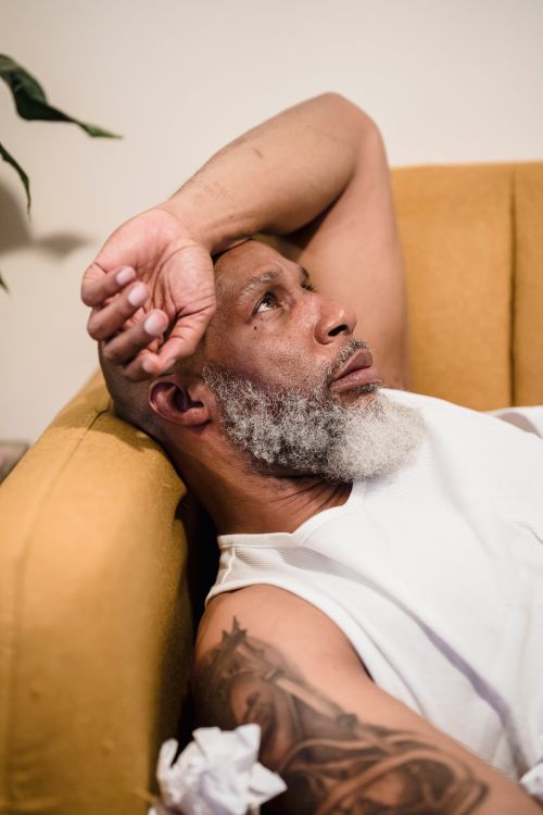 Free Elderly man with a beard looking contemplative while lying on a couch at home. Stock Photo
