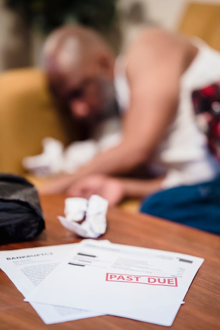 Unpaid Bills On A Table And A Distraught Man In Background