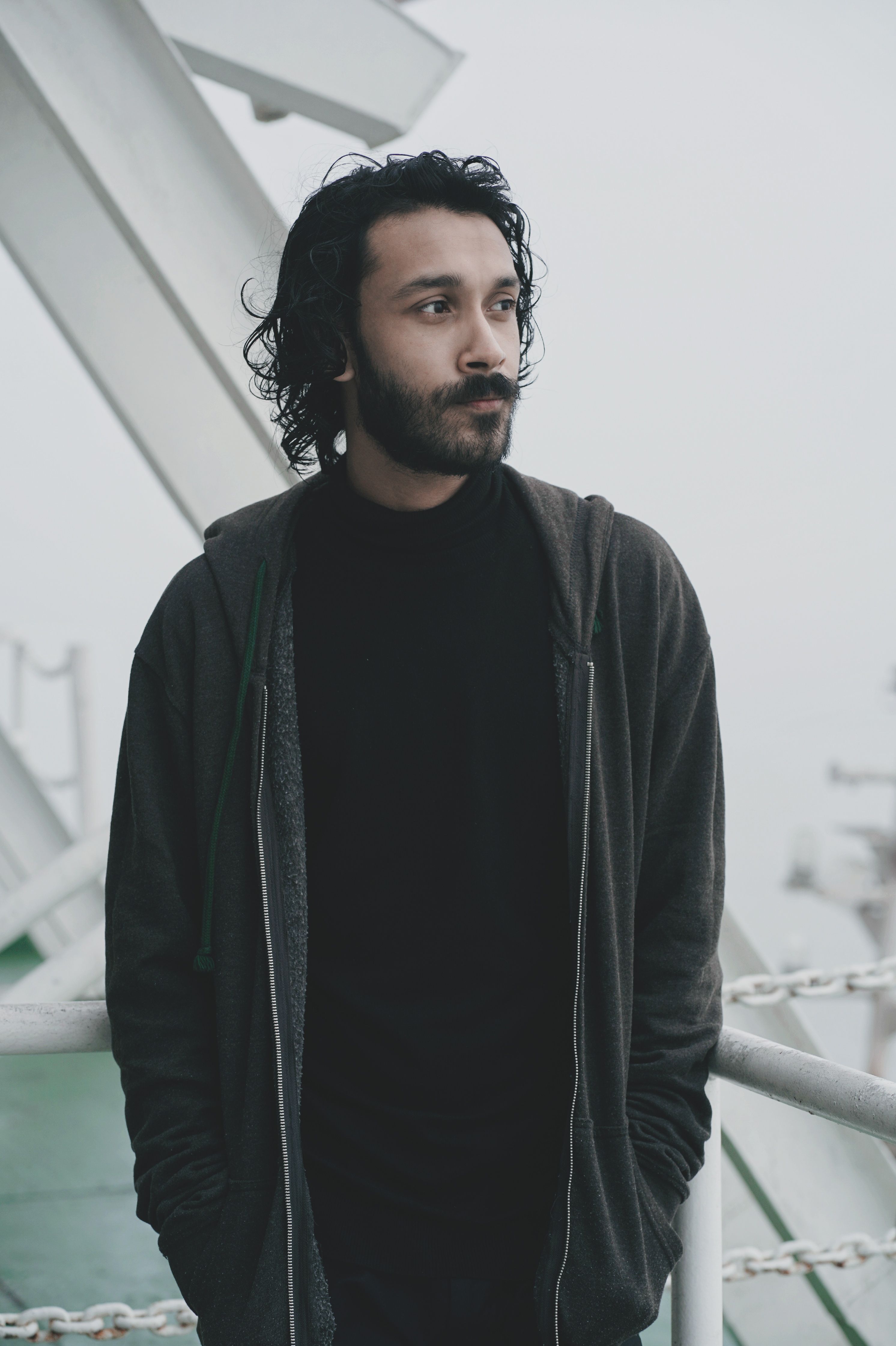 A thoughtful man with facial hair standing outdoors on a cloudy day, exuding a contemplative vibe.