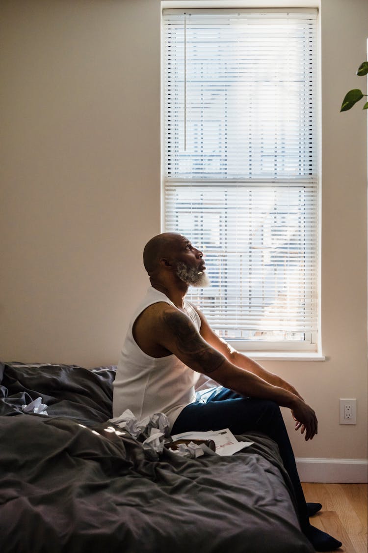 Old Man Sitting On Bed Stressed With Documents