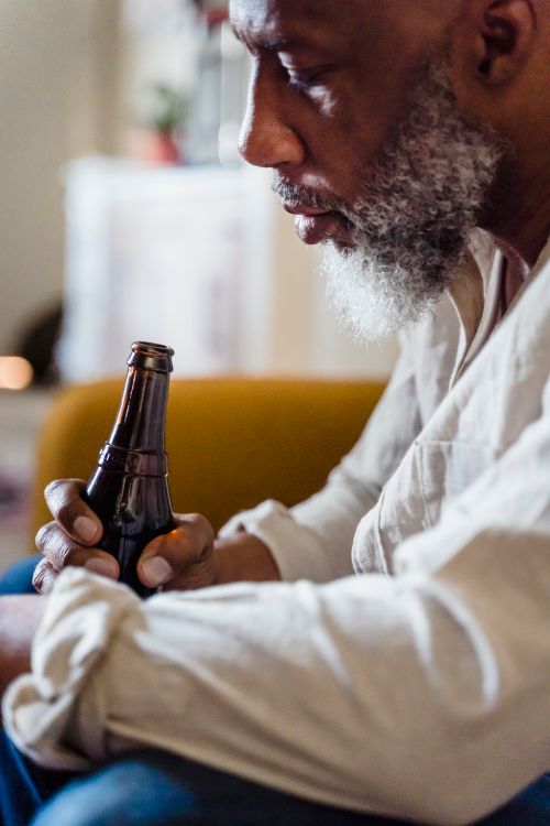 Free Thoughtful elderly man sits indoors holding a bottle of beer. Stock Photo