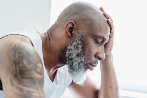 Free Profile of a bald, bearded man deep in thought, hand on forehead, tattoo visible. Stock Photo