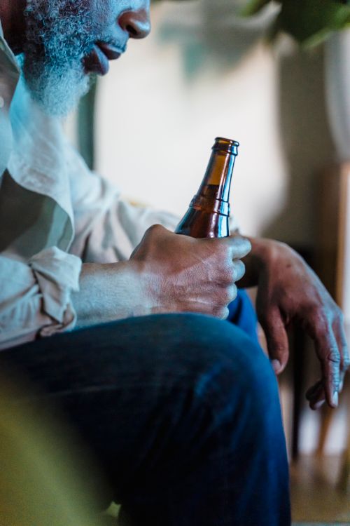 Free A man sitting indoors holding a beer bottle, with partial focus on his hands and bottle. Stock Photo