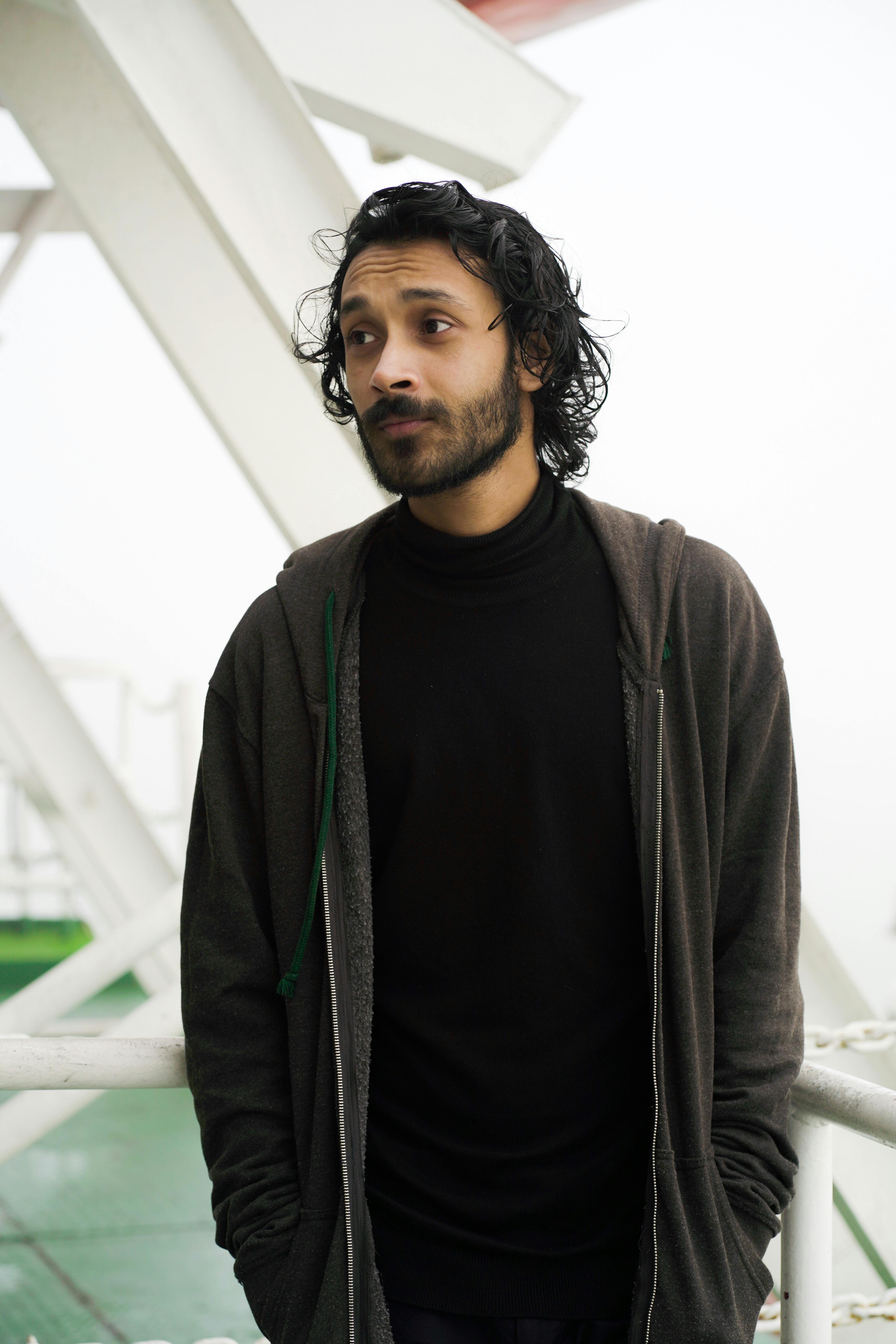 A contemplative man with facial hair standing outdoors in an urban environment.