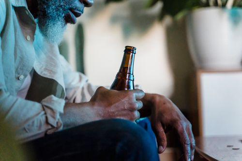 Free Close-up of a thoughtful man holding a beer bottle in a relaxed indoor setting. Stock Photo