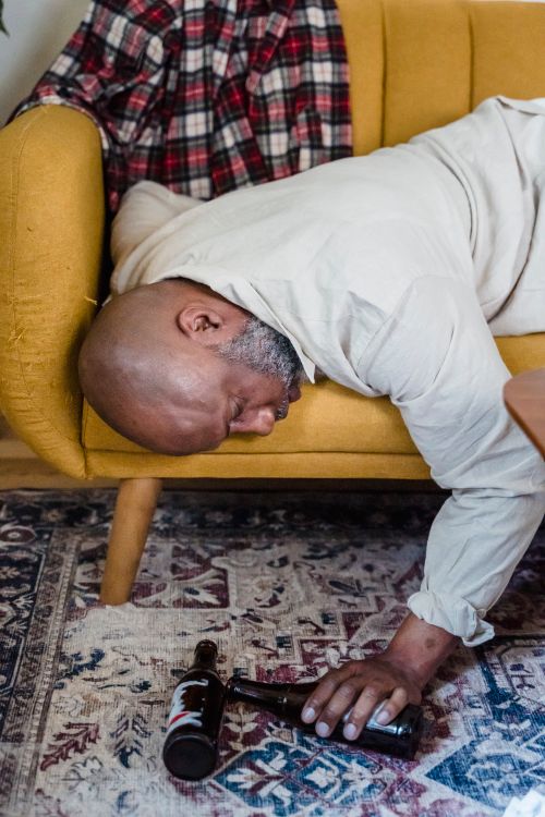 Free African American man sleeping on a mustard couch with bottles on the floor. Stock Photo