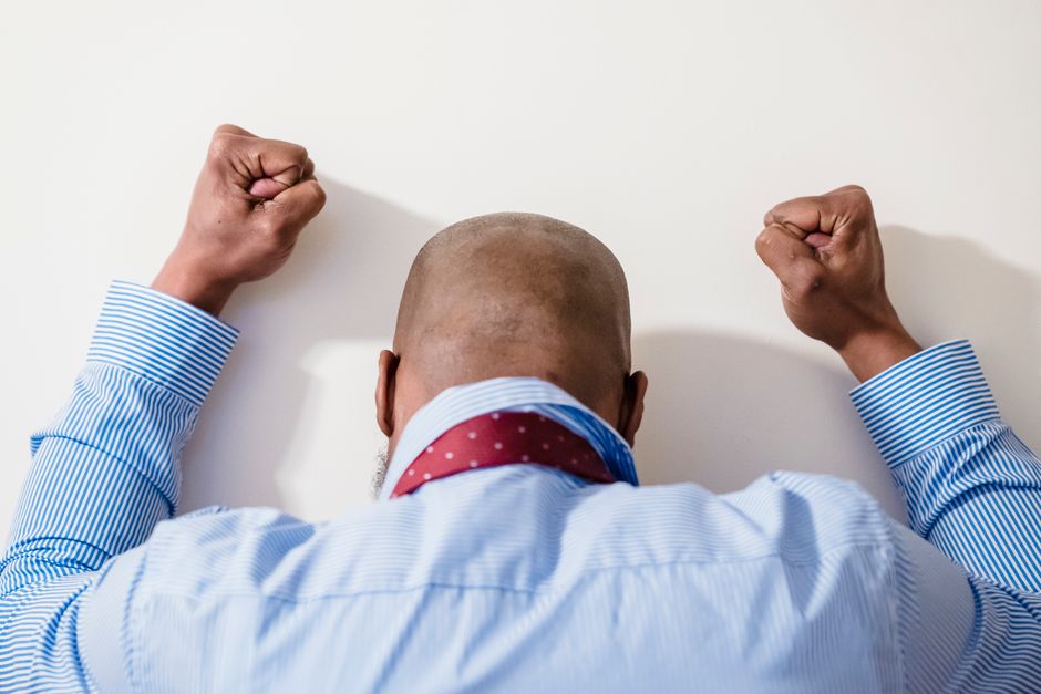 A bald man in a blue striped shirt with clenched fists expressing frustration against a white background. A bald man in a blue striped shirt with clenched fists expressing frustration against a white background.