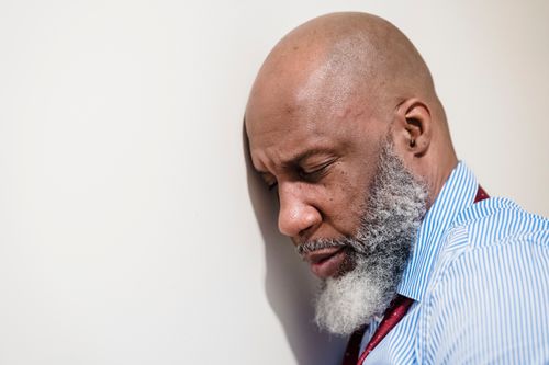 Free A thoughtful bald man with a beard leaning against a white wall. Emotional portrait. Stock Photo