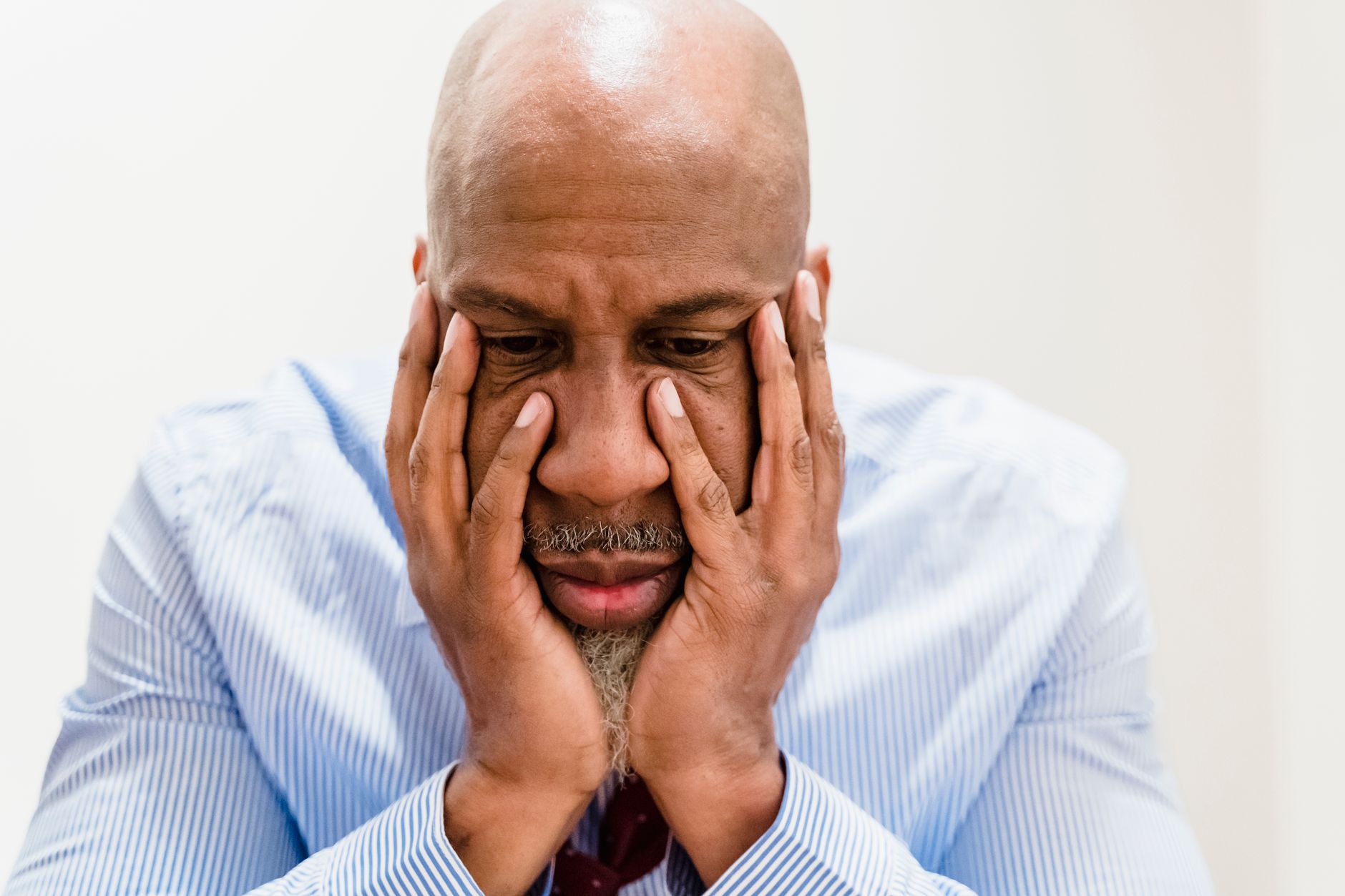 A bald man in a striped shirt poses with hands on face, deep in thought.