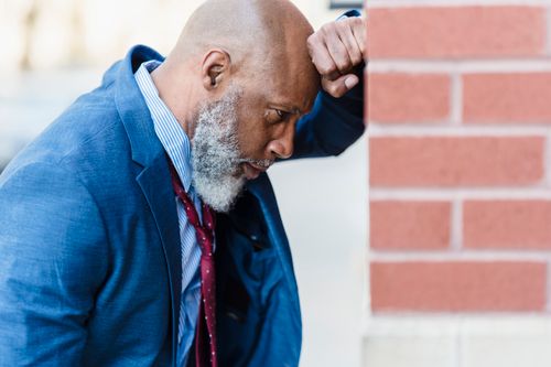 Free A thoughtful businessman in a blue suit is seen leaning against a brick wall, looking pensive outdoors. Stock Photo