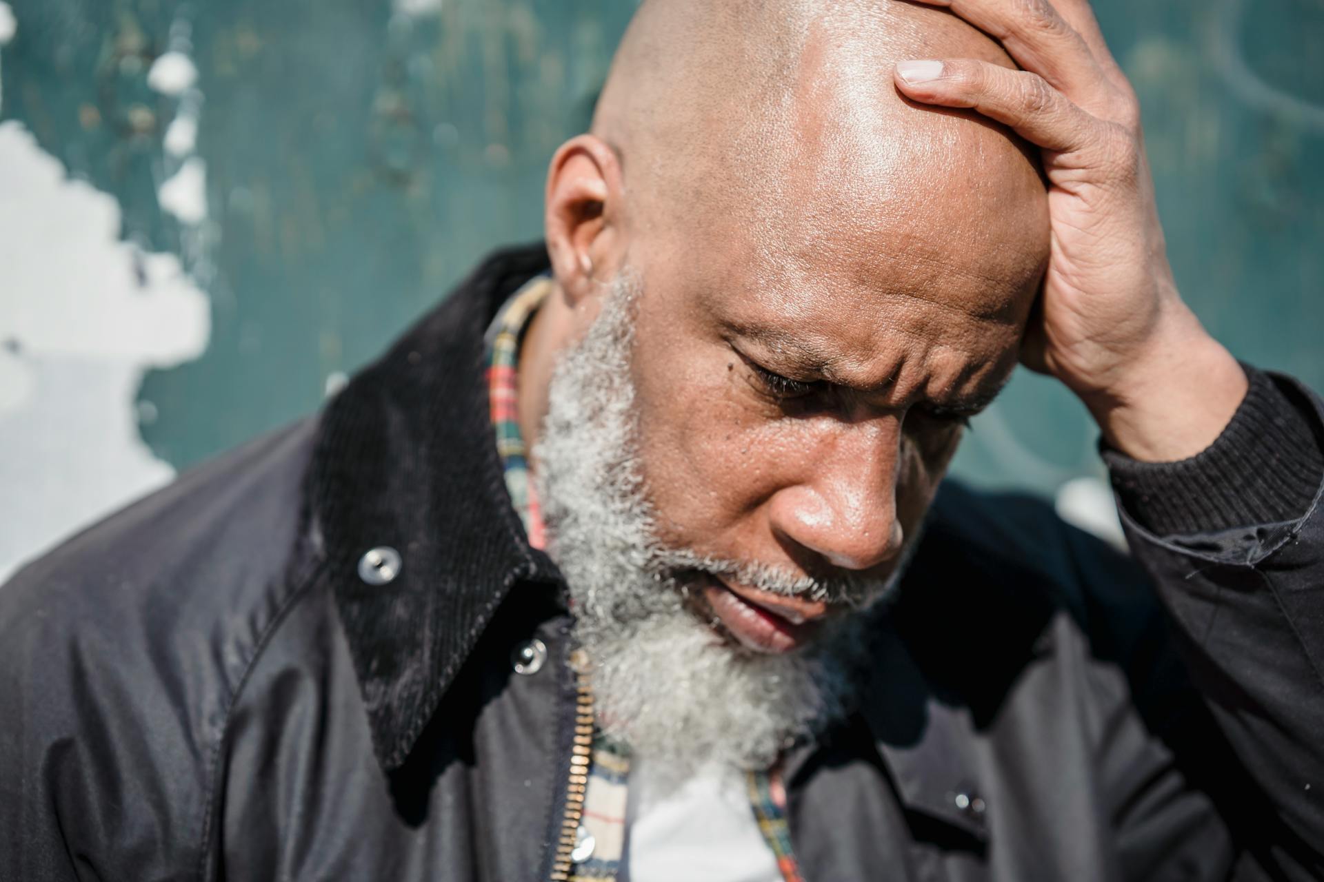 Senior man in deep thought outdoors, holding his head with a serious expression.