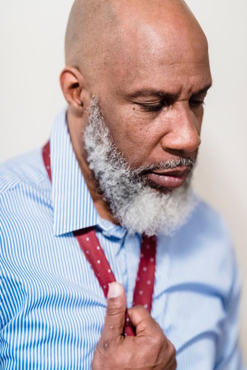 Free Close-up portrait of a mature man adjusting his tie with a contemplative expression and a stylish beard. Stock Photo