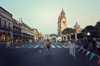 白天，一名马拉松运动员大步穿过城市街道，街道位于一座历史悠久的大教堂前，两旁是欢呼的人群