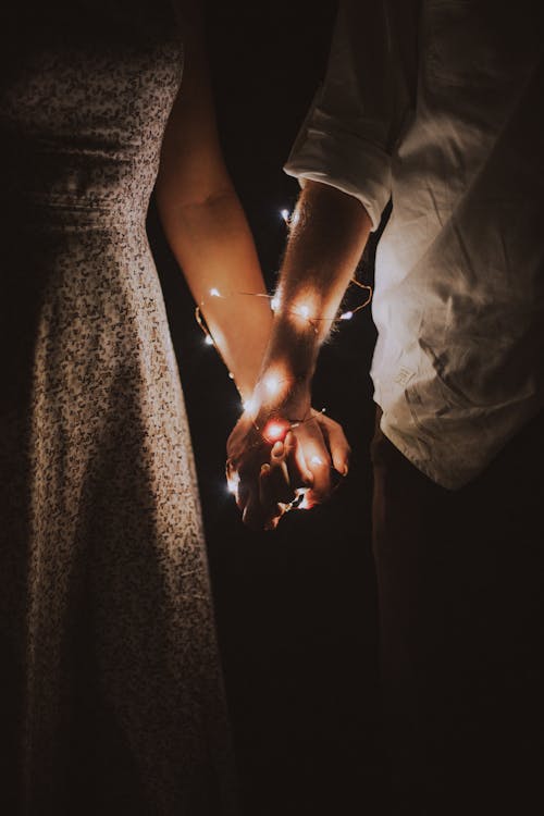 Мужчина и женщина держатся за руки, обмотанные гирляндами