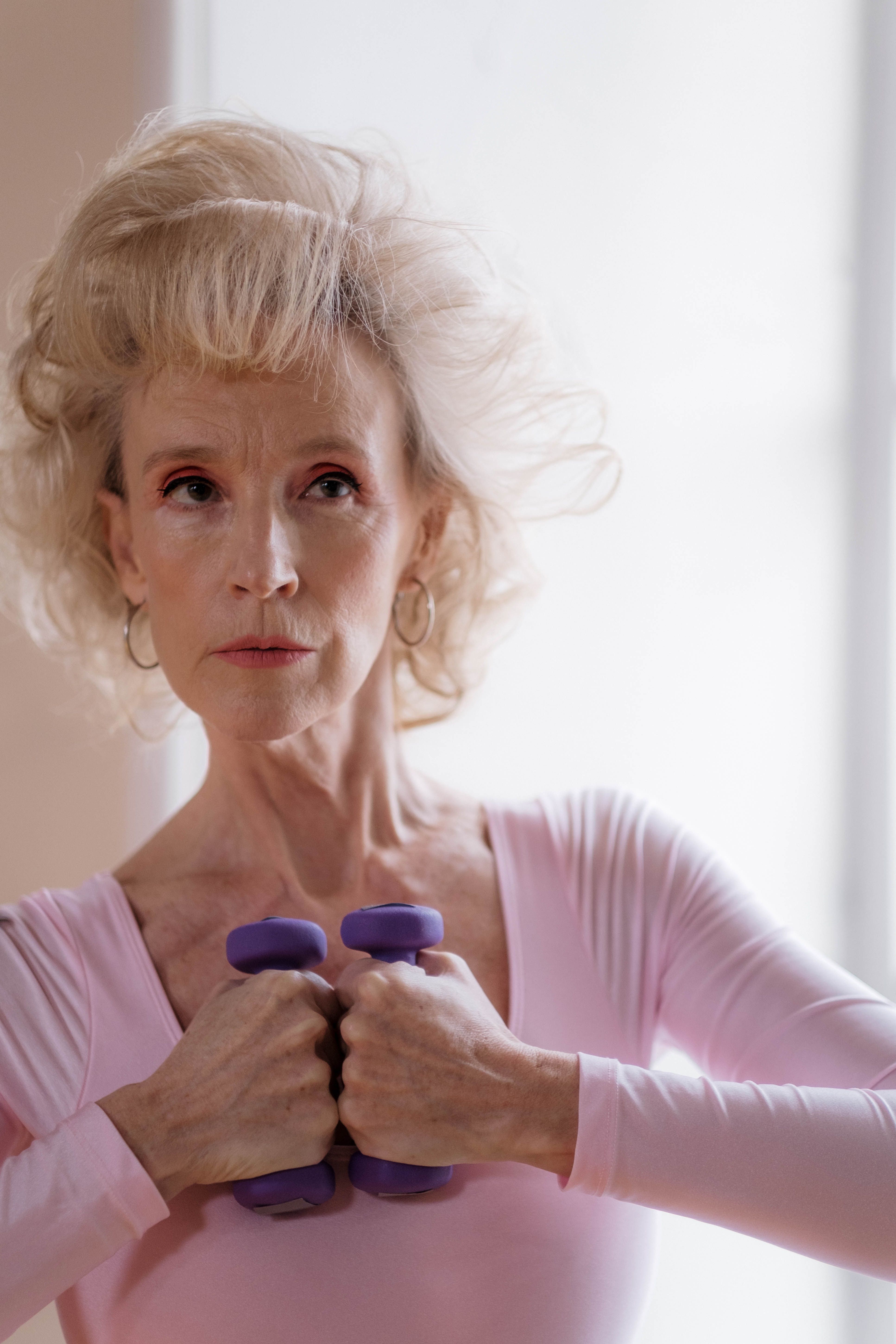 Senior woman in pink outfit exercising with dumbbells indoors, focused expression.