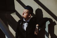 穿着西装的年轻人闭着眼睛享受阳光，在室内投下戏剧性的阴影