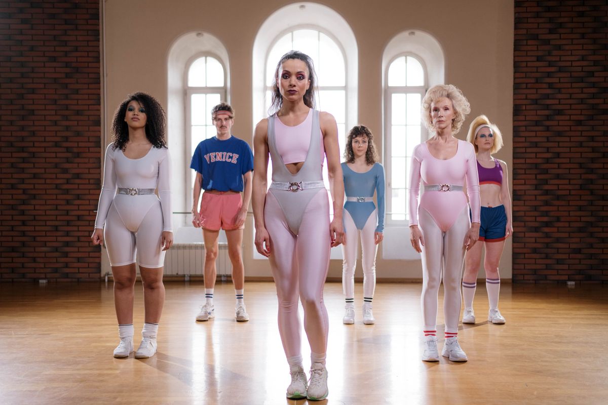 Group of adults wearing retro aerobics outfits in a bright dance studio