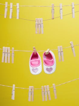 一双可爱的粉色心形婴儿鞋用晾衣夹挂在黄色背景上