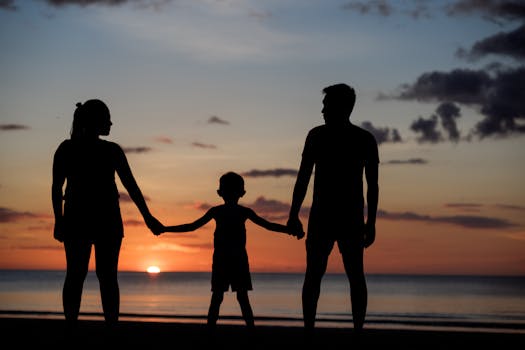 A silhouette of a family holding hands on a beach during a beautiful sunset.