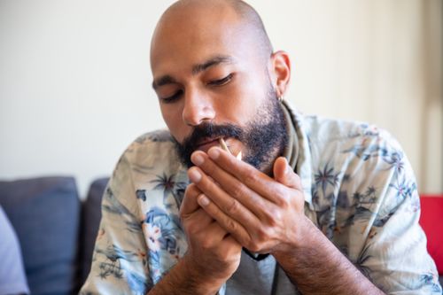 Free A bald man with a beard lights a cigarette indoors, focused and contemplative. Stock Photo
