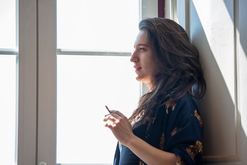 Free A thoughtful woman stands by a window, enjoying a moment of relaxation indoors. Stock Photo