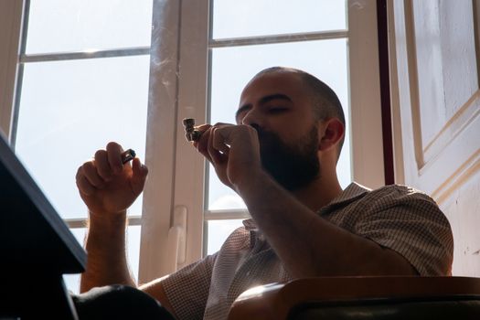 A bearded man smoking a pipe indoors, showcasing a relaxed and contemplative moment.