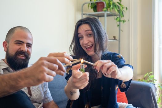 A man and woman laughing while lighting a joint indoors, showcasing a relaxed lifestyle.