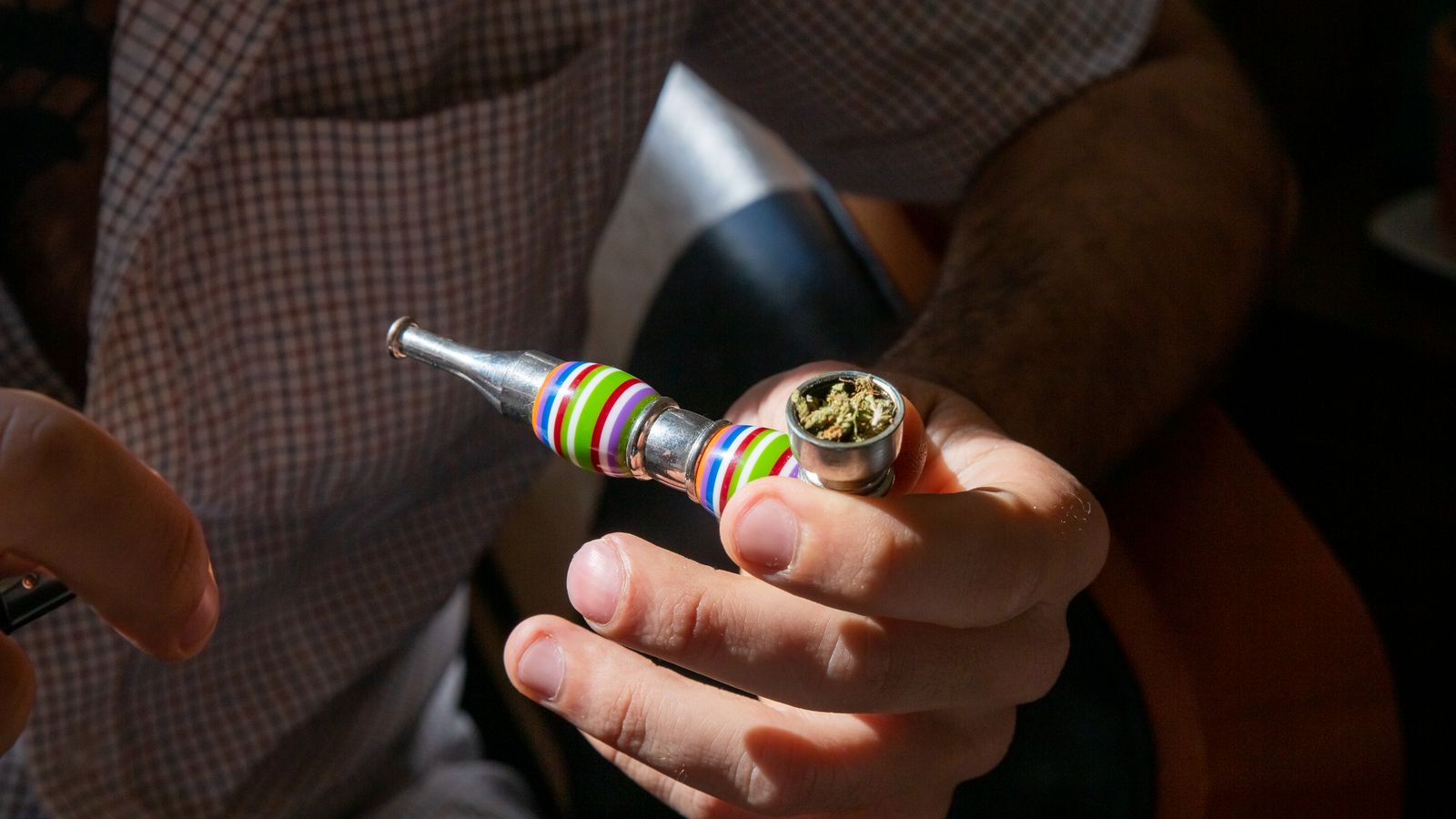 Adult holding a colorful pipe containing cannabis indoors with natural light.