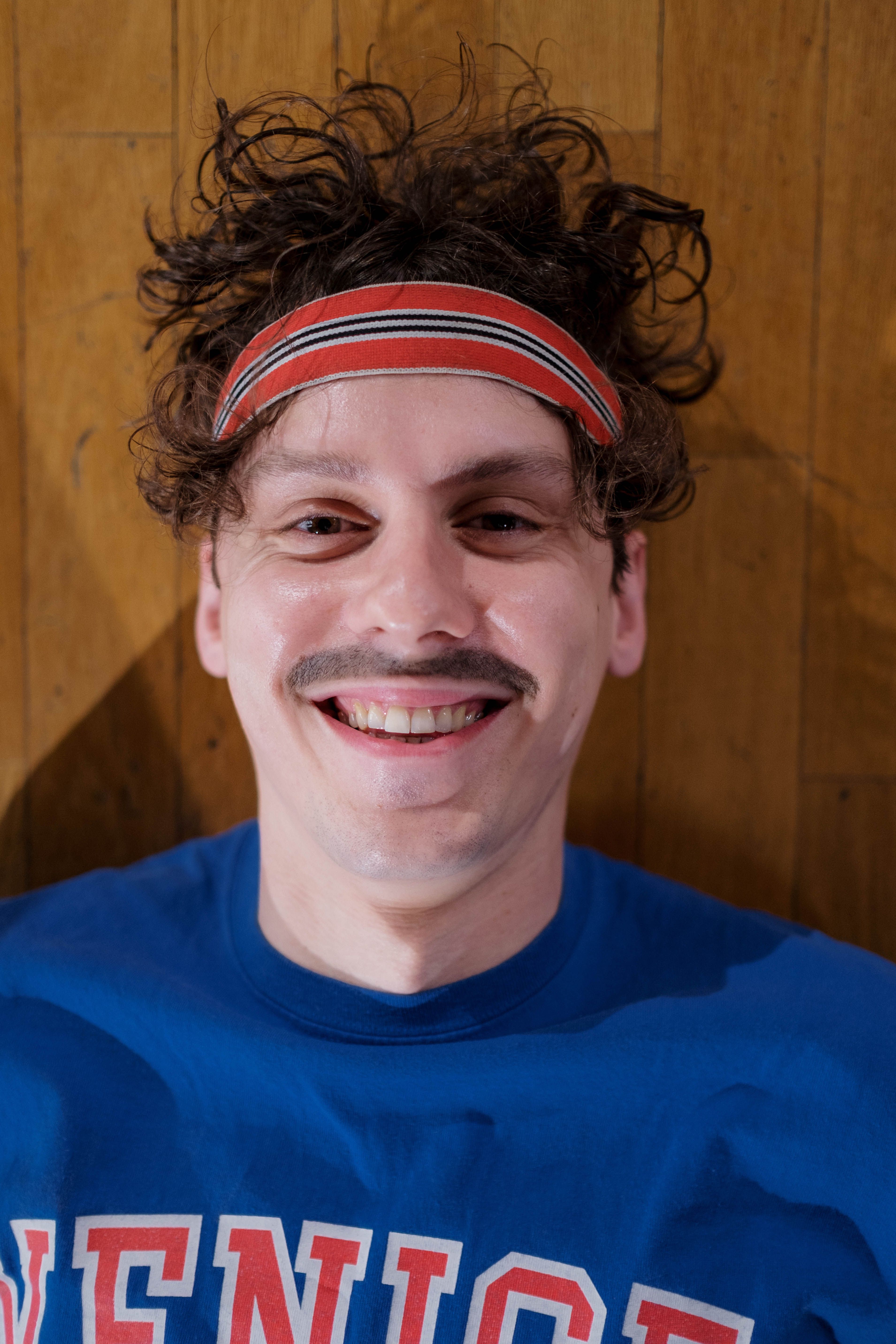 Cheerful man in a headband smiling while lying on a wooden gym floor.