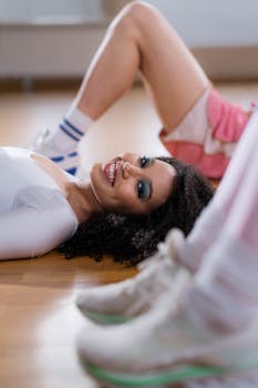 Woman with curly hair on floor in fitness setting, smiling brightly.