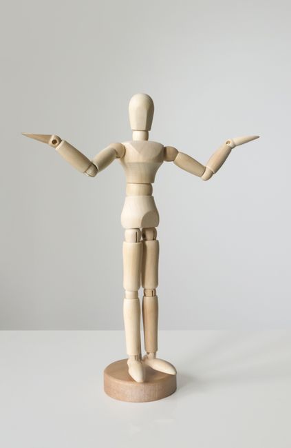 A minimalist wooden mannequin with open arms on a white surface, perfect for artistic expression concepts.