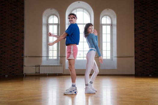 A retro-themed fitness duo poses energetically in a spacious dance studio.