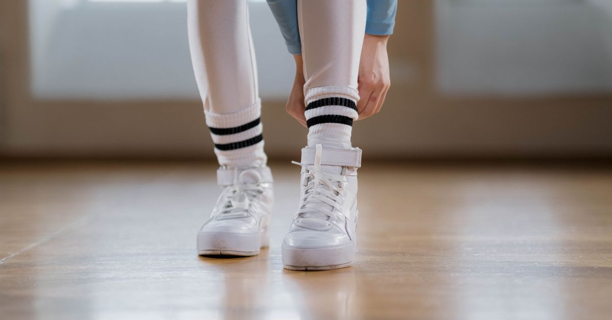 Close-up of a person tying white sneakers indoors, wearing leggings and striped socks.