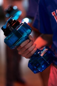 Focused close-up of a person gripping a blue dumbbell, emphasizing fitness and exercise in a gym setting.