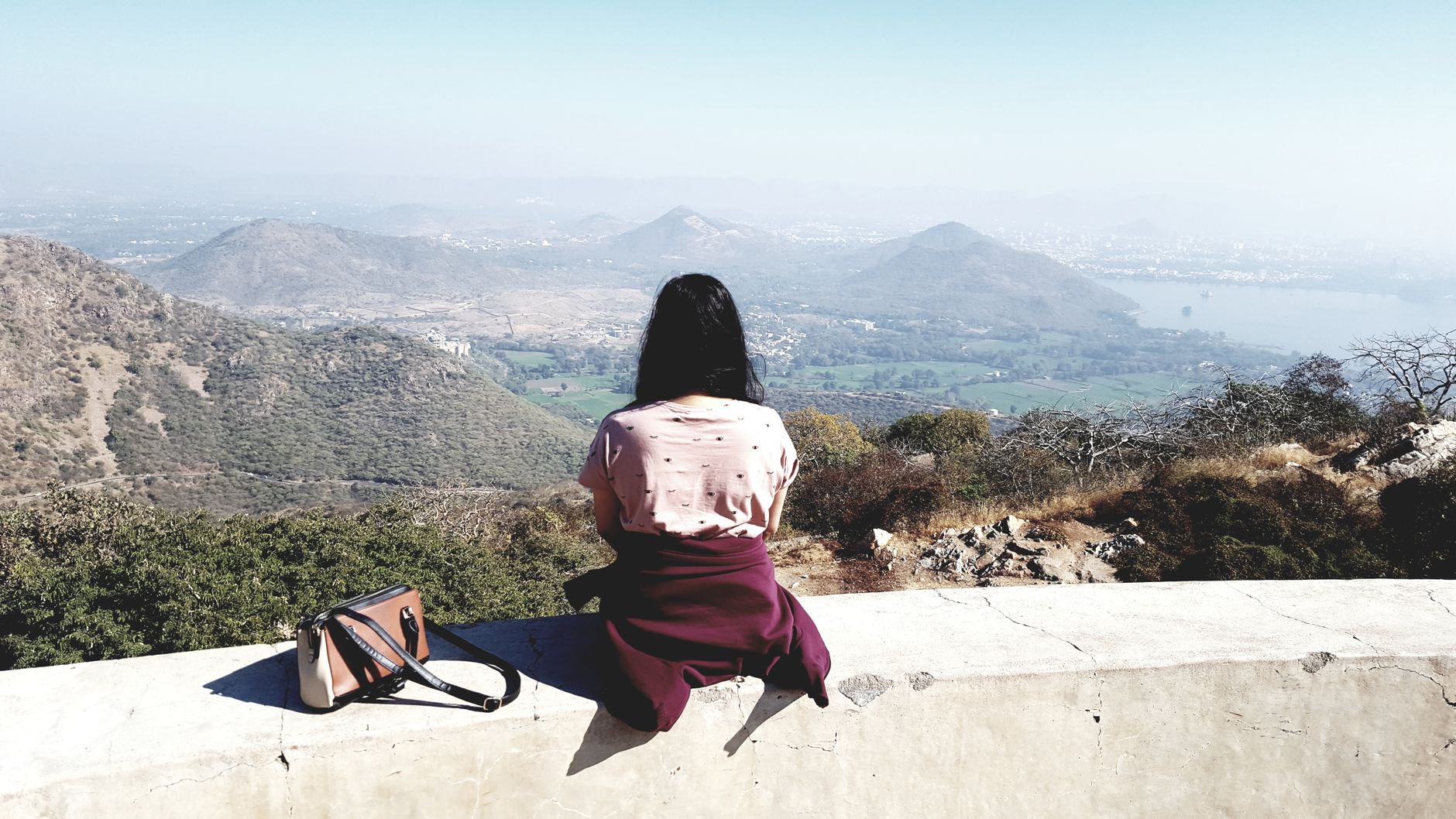 A woman sits on a wall, overlooking the scenic landscape of Kodiyat, India.