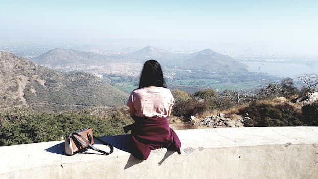 A woman sits on a wall, overlooking the scenic landscape of Kodiyat, India.