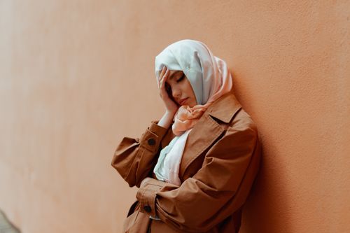 Free A woman in a hijab leans against an orange wall, lost in thought with closed eyes. Stock Photo
