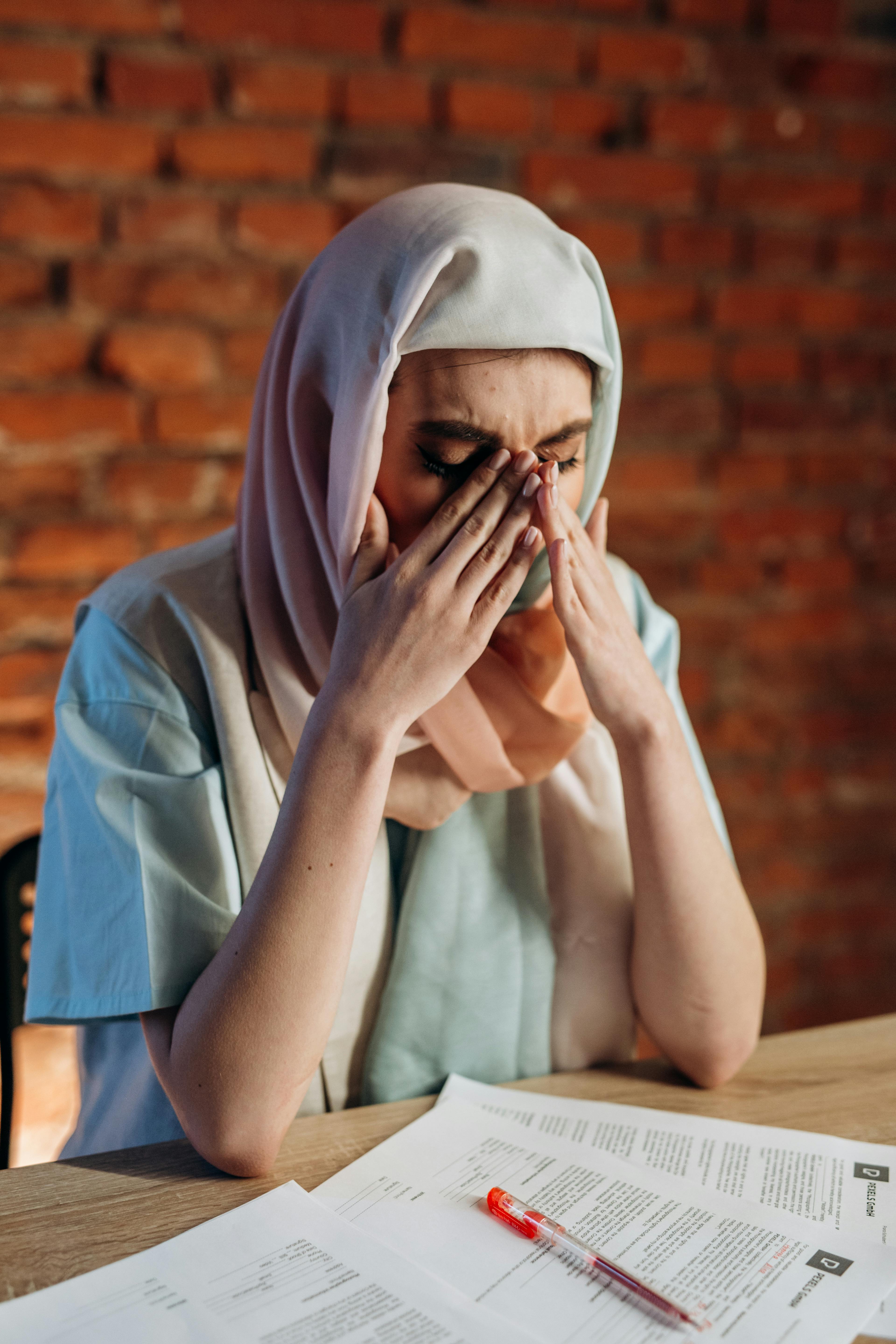 Middle Eastern woman in hijab looking stressed at work desk.