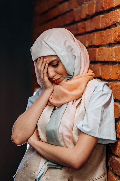 Free A woman in a hijab leans against a brick wall, portraying deep thought and emotion. Stock Photo