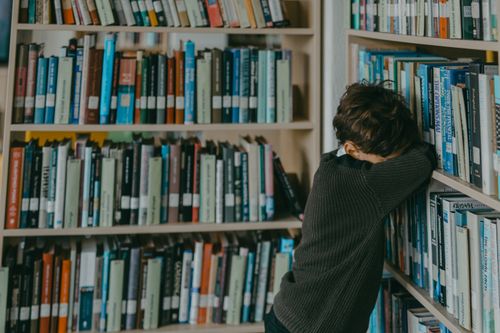 Free Young boy in a library, resting against a bookshelf, wearing a knitted sweater. Stock Photo