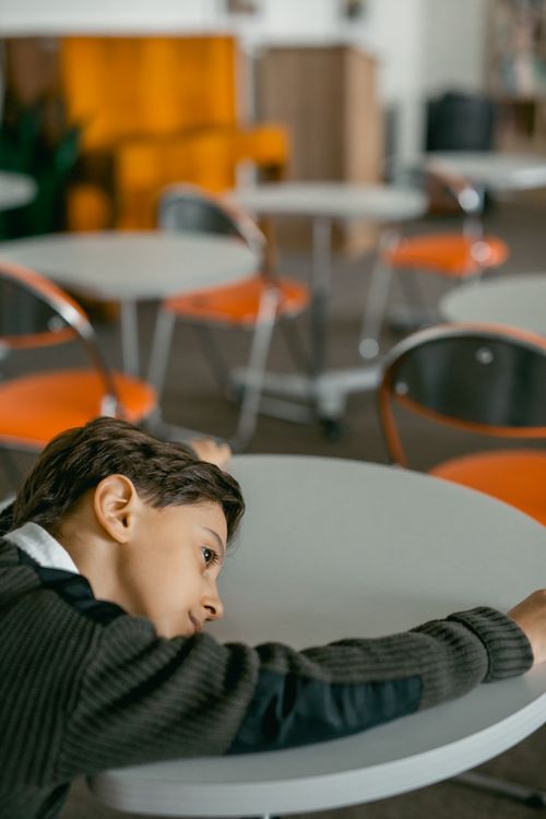 Free A young boy appears sad in an empty classroom, expressing loneliness and vulnerability. Stock Photo