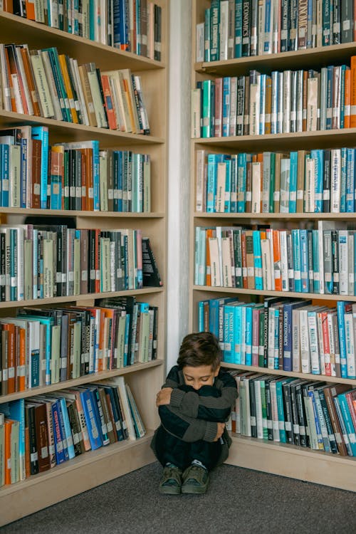Lonely Boy in Gray Sweater Sitting and Leaning Against Bookshelves