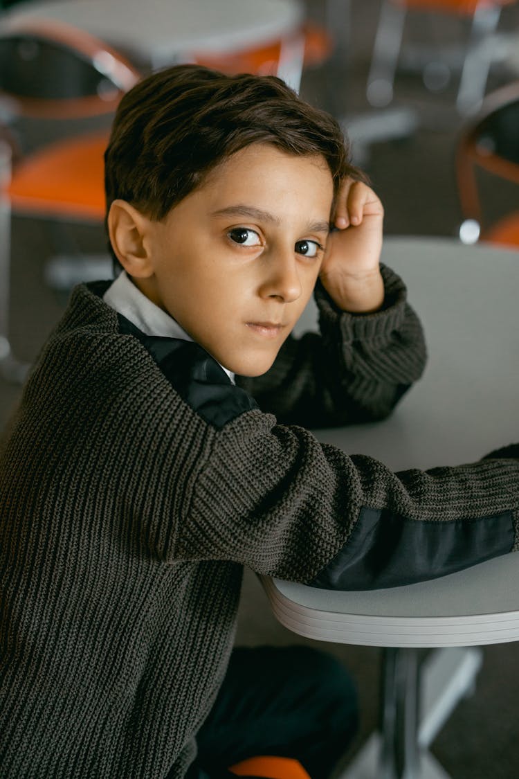 Lonely Boy In Gray Sweater Sitting Inside A Classroom