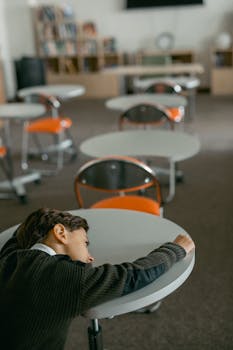 A young boy rests on a desk in an empty classroom, showcasing a contemplative mood.